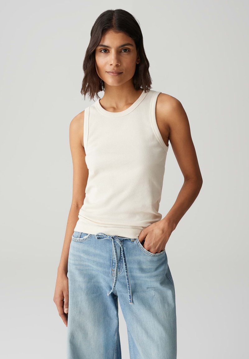 Top in cotone ribbed beige chiaro con scollatura tonda, design senza maniche e finitura elastica sull'orlo, abbinato a jeans a gamba larga blu chiaro.