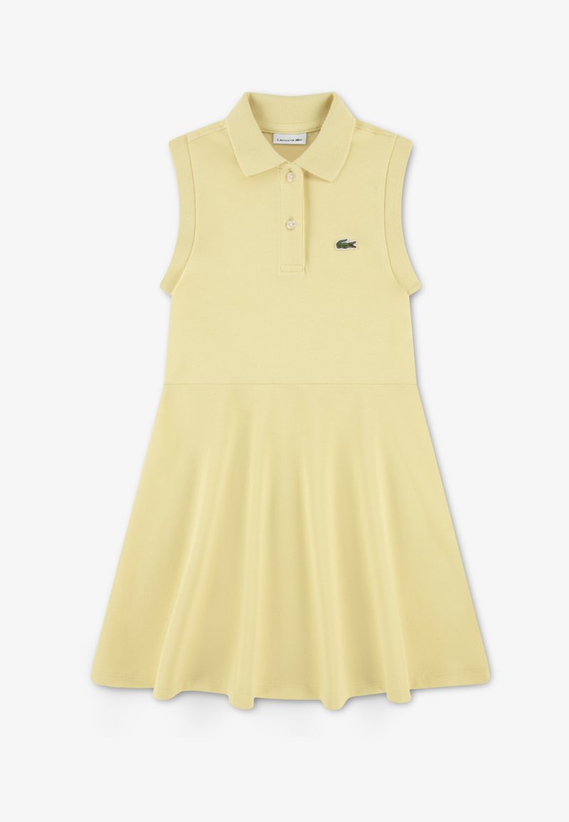 Φόρεμα πόλο σε ανοιχτό κίτρινο βαμβάκι με αμάνικο σχέδιο, γιακά και φούστα σε φαρδιά γραμμή. Διαθέτει πράσινο λογότυπο ως διακοσμητικό στοιχείο.