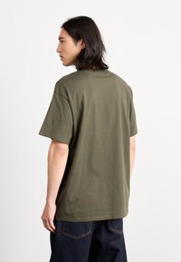 Olivgrön bomulls T-shirt med kort ärm, rund halsringning och avslappnad passform, bärs med mörk denimbyxor. Enfärgad design, utan mönster.