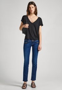 Black v-neck t-shirt with short sleeves, paired with fitted blue jeans and strappy black sandals, held a black bag in the left hand.