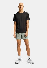 Camisa deportiva negra de manga corta, pantalones cortos verde claro, zapatillas blancas con detalles negros, diseño sencillo, tejido ligero.