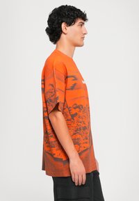 Orange grafisk t-shirt med et landskabsdesign, korte ærmer og rund halsudskæring. Lavet af bomuld, med en afslappet pasform og synlige sømme.