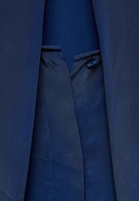 Giacca in tessuto blu navy in primo piano, con una texture liscia, un dettaglio con bottone e una fodera interna senza cuciture con uno schema di colori coerente.