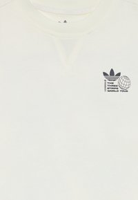 Krēmkrāsas sporta krekls ar plakanu apkakli, ar mazu melnu logotipu un globusa grafiku kreisajā krūtīs. Mīksta tekstūra ar ribotām piedurknēm.