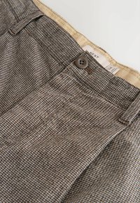 Brown patterned trousers with a textured weave, featuring a front button closure and a label visible inside the waistband.