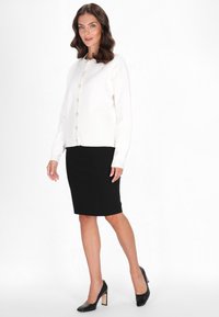 Weißer Strickcardigan mit Rundhalsausschnitt und sieben Knöpfen, kombiniert mit einem figurschmeichelnden schwarzen Bleistiftrock und schwarzen High Heels.