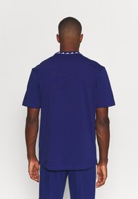 Camiseta de manga corta azul marino hecha de algodón. El diseño en la parte posterior presenta un acento de logo blanco en el cuello. Textura suave, corte relajado.