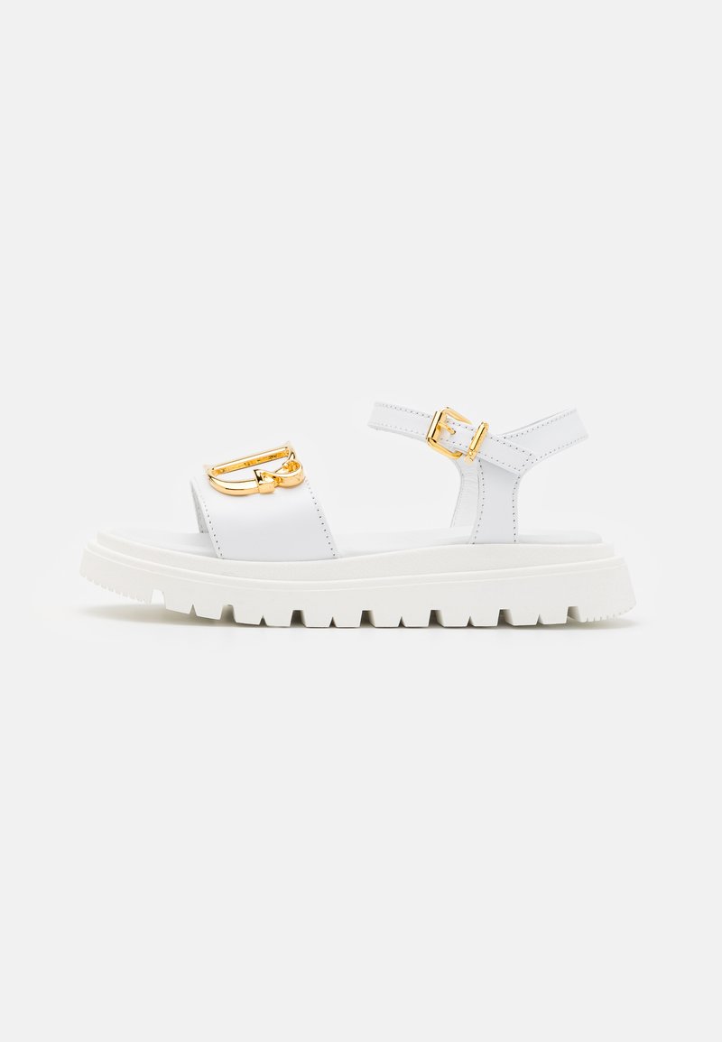 Sandalino bianco con suola spessa, dotato di accessori in oro, cintura regolabile alla caviglia e tomaia liscia dal design minimalista.