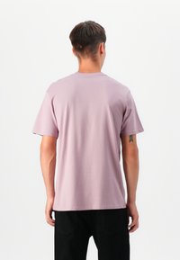 Lyselilla crew-neck t-skjorte laget av mykt stoff, med korte ermer og en avslappet passform. Bakre visning viser jevn tekstur og enkelt design.