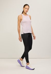 Lichtroze mouwloos tanktop met zijsplitten, gecombineerd met zwarte leggings en hardloopschoenen met paarse accenten. Soepele stof en getailleerd ontwerp.