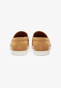 Bež nubuk slip-on cipele s niskim profilom, bijelim gumeni đonom i minimalnim detaljima šivanja. Zaobljena peta i glatka tekstura.