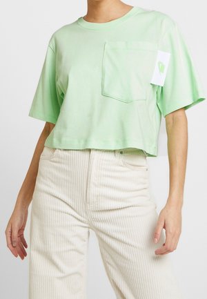 Mintgrøn cropped t-shirt i letvægtsbomuld med rund hals, korte ærmer og en lomme foran. Tag synligt på siden.