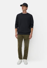 Marine Sweatshirt mit gerippten Bündchen, olivfarbene Cordhose und weißen Sneakers. Die Cap ist dunkel und hat ein dezentes Logo auf der Vorderseite.