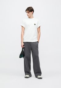 Λευκό βαμβακερό t-shirt με γυρισμένα μανίκια και τσεπή στο στήθος, συνδυασμένο με άνετο γκρι φόρμας παντελόνι και γκρι-μαύρα αθλητικά παπούτσια.