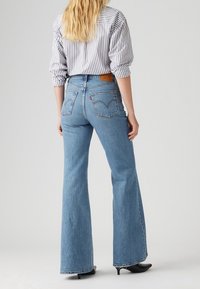 Vaqueros acampanados de mezclilla en azul claro, con cintura alta, bolsillos traseros con detalles de costura y una parche de cuero marrón en la cinturilla.