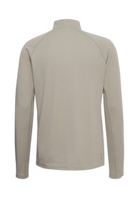 Langärmeliges Hemd in hellbeige mit strukturiertem, hexagonalem Muster. Verfügt über einen hohen Kragen und Raglanärmel für Bewegungsfreiheit.