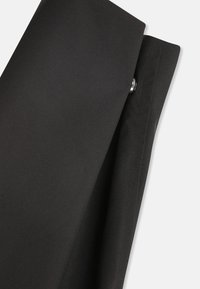 Tessuto nero con una texture liscia, caratterizzato da una piega e un accento di bottone argento sul lato. Linee semplici e pulite con un design minimale.