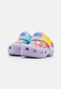 Zuecos morados para niños con correas temáticas de Peppa Pig coloridas y decoraciones de dibujos animados sobre un fondo blanco.