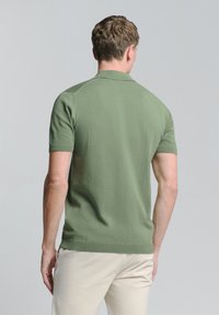 Olijfgroene polo met korte mouwen, gemaakt van een gladde stof, met een geribbelde kraag en zoom. Van achter bekeken, waarbij het aansluitende ontwerp en de schouders zichtbaar zijn.