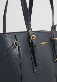 Laadukkaasta nahasta valmistettu laivastonsininen kassi, jossa on teksturoitu pinta, kultasävyiset yksityiskohdat, kaksoiskahvat ja turvalliset lukot lisäämään käyttömukavuutta.