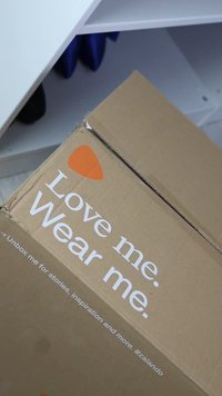Brown cardboard box with white text saying "Love me. Wear me." and an orange accent. Box is closed, with visible edges and a smooth texture.