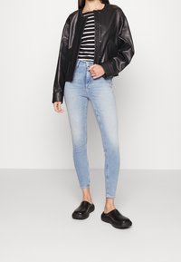 Chaqueta bomber de piel negra, camiseta rayada, jeans skinny azul claro y zapatos negros sin cordones. Textura suave y diseño ajustado.
