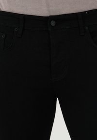 Svarta denimjeans med en slät yta, femfickdesign och en enkel knappstängning. Sömmarna står i svag kontrast till tyget.