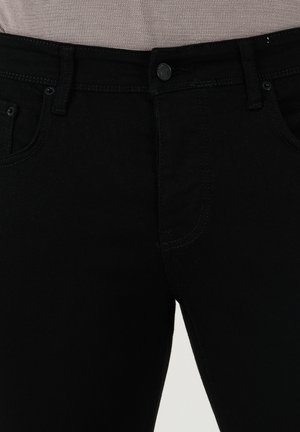 Jeans in denim nero con una texture liscia, design a cinque tasche e chiusura con un solo bottone. La cucitura contrasta leggermente con il tessuto.