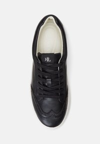 Black leather sneaker with a white rubber sole, featuring round laces, brogue detailing, and a textile lining with brand logo on the tongue.