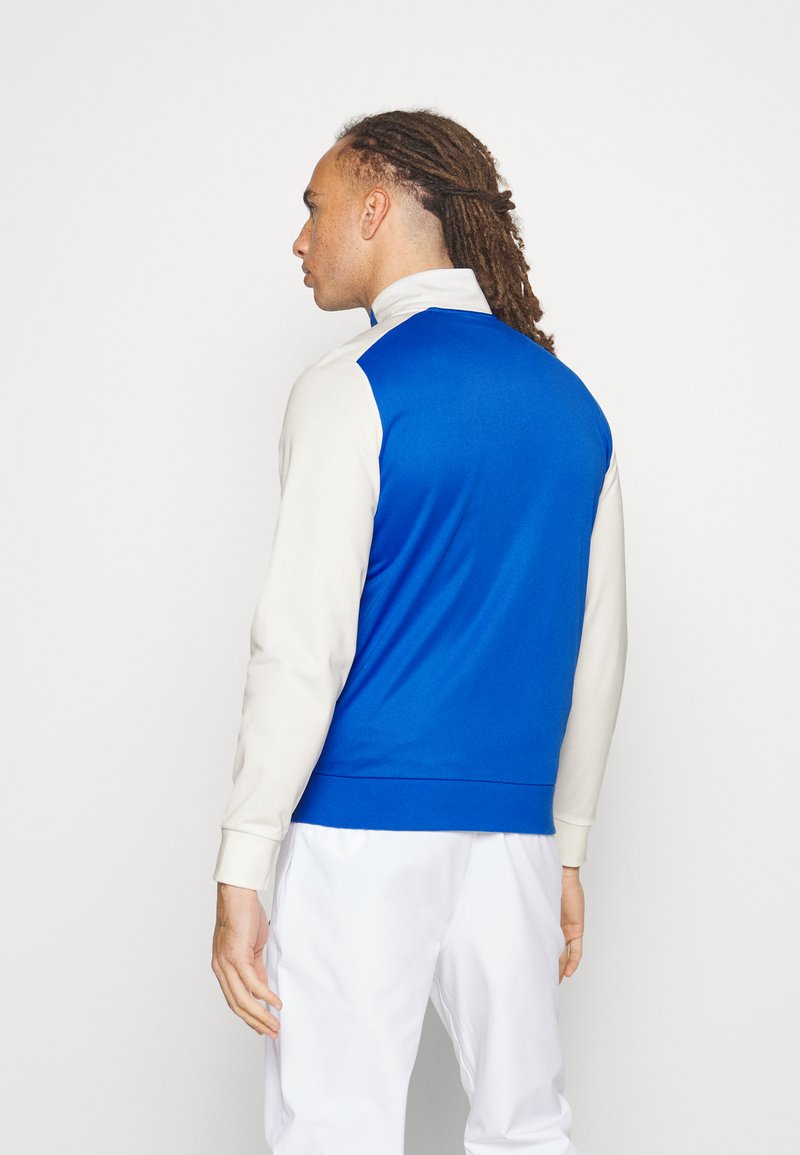 Niebieski i kremowy sweter z wysokim kołnierzem, rękawami raglanowymi i dopasowaną talią. Gładki materiał o czystym, minimalistycznym designie.