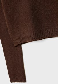 Manche et ourlet d'un pull en maille brun foncé avec poignets et ceinture côtelés sur un fond clair.