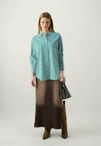 Striped turquoise button-up shirt, brown gradient maxi skirt, knee-high brown boots, and a small black and white handbag.