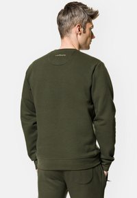 Oliwkowy dres z prążkowanymi mankietami i dołem. Posiada okrągły dekolt oraz dyskretną metkę na górnej części pleców. Wykonany z miękkiego, teksturowanego materiału.