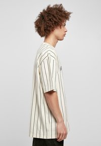 Cremefarvet stribet t-shirt med korte ærmer, der har sorte lodrette striber, en afslappet pasform og en blød bomuldsstruktur.