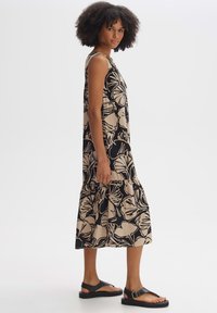Black and beige floral patterned sleeveless dress with a tiered hem, made of lightweight fabric, paired with black flat sandals.