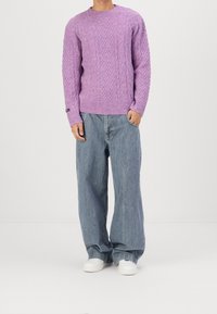 Lila neulottu neule, jossa on teksturoitu kuvio, pyöreä kaula-aukko ja resorireunukset, yhdistettynä löysiin, vaaleansinisiiin farkkuihin ja valkoisiin tennareihin.