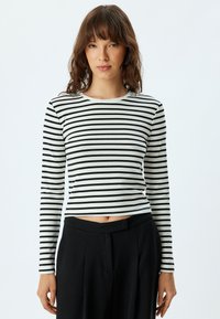 Schwarz-weiße gestreifte langärmelige Bluse mit rundem Ausschnitt und figurbetontem Schnitt, kombiniert mit hoch taillierten schwarzen Hosen.