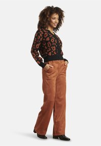 Black cardigan with orange leopard print, button closure, paired with rust-colored suede pants and black heeled boots.