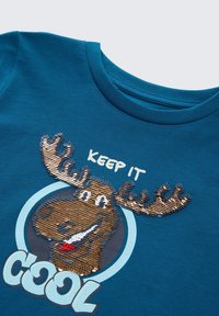 Cămașă albastră cu o față zâmbitoare de rezervă din paiete reversible și textul "MENȚINE-L RĂCROSS" sub capul moose-ului.