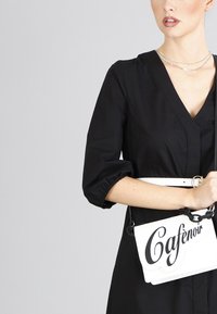 Sort kjole med puffede ærmer og V-udskæring, parret med en hvid taske med sort tekst "Cafenor" og en kædesti.