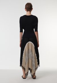 Top negro de canalé con mangas cortas, combinado con una falda plisada beige con detalles de encaje negro y un dobladillo ondulado.