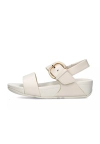 Beige sandaal met verstelbare enkelband, voorzien van een gouden gesp, brede teband en een witte platformzool. Gladde lederen textuur.