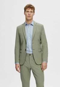 Light green suit made of smooth fabric, featuring a single-breasted blazer, notch lapels, and contrasting blue shirt underneath.