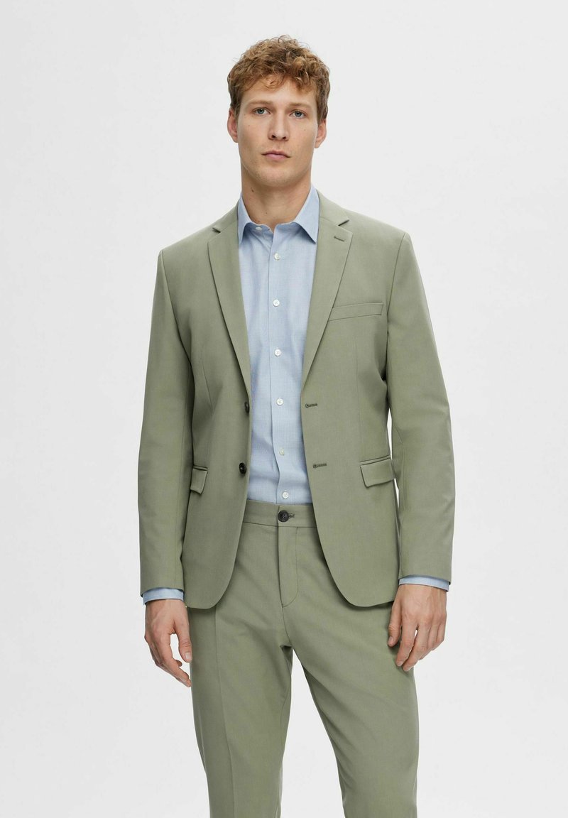 Light green suit made of smooth fabric, featuring a single-breasted blazer, notch lapels, and contrasting blue shirt underneath.