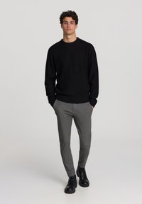 Maglione nero lavorato a maglia, pantaloni grigi e stivali neri con lacci. Il maglione presenta un collo a giro e polsini a coste. Tessuto neutro e strutturato.