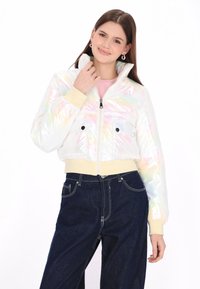 Irideszcens, rövidített fazonú dzseki magas gallérral, két elülső zsebbel, bézs bordázott mandzsettával és szegéllyel. Rózsaszín felső fölött és sötét farmerruhával viselve.