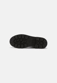 Suela de zapato de goma negra con surcos profundos para tracción, logo en relieve y una textura lisa con un diseño de punta redondeada.