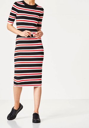 Musta, punainen ja valkoinen raidallinen neulemekko, jossa on lyhyet hihat ja vartalonmyötäinen siluetti; yhdistetty mustiin tennareihin.