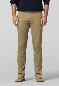 Beige chinos med en glat tekstur, tapered fit og forlommer. Båret med lysebrune ruskinds loafers. Ribbede navy sweater ovenfor.