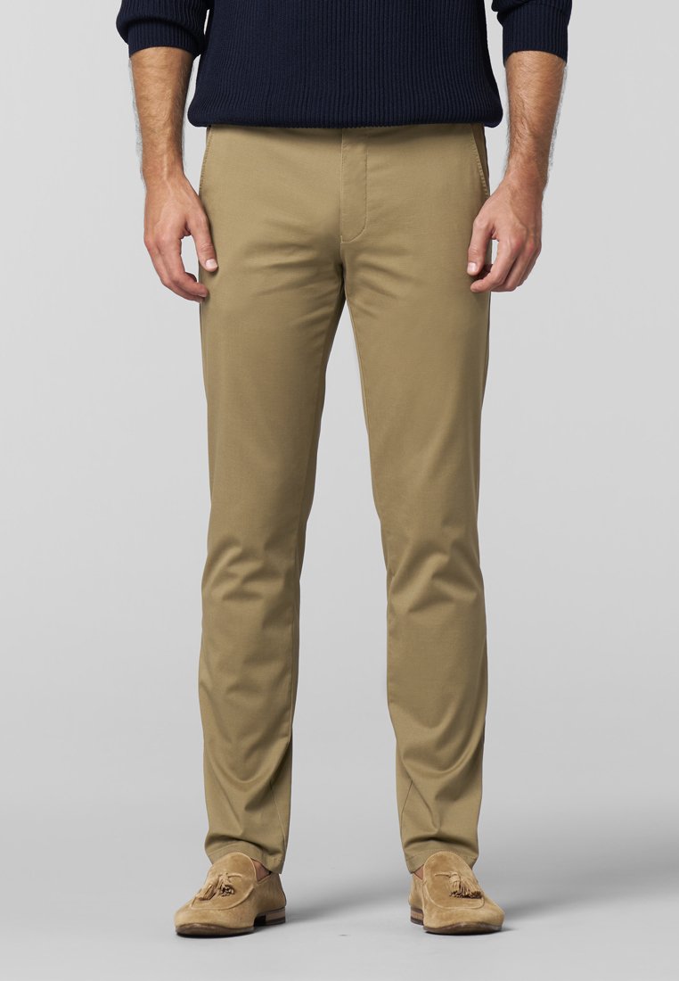 Beige chinos med en glat tekstur, tapered fit og forlommer. Båret med lysebrune ruskinds loafers. Ribbede navy sweater ovenfor.